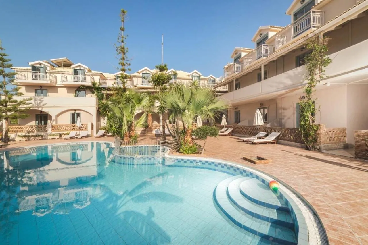 Piscine turquoise entourée de transats et de végétation luxuriante devant un bâtiment beige.