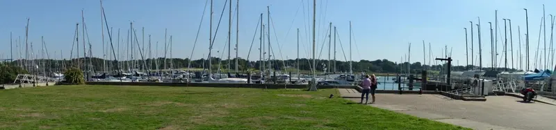 Vue panoramique sur un port de plaisance ensoleillé avec des bateaux à quai et une pelouse verdoyante.