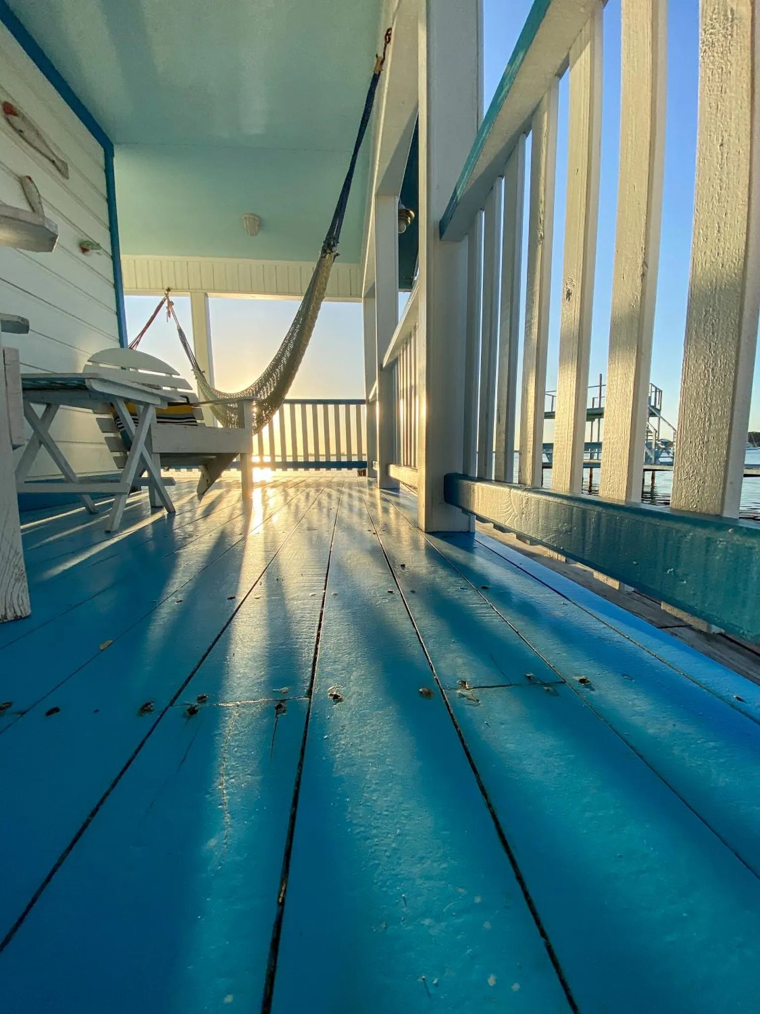 Terrasse en bois bleu avec un hamac suspendu et une vue sur la mer.