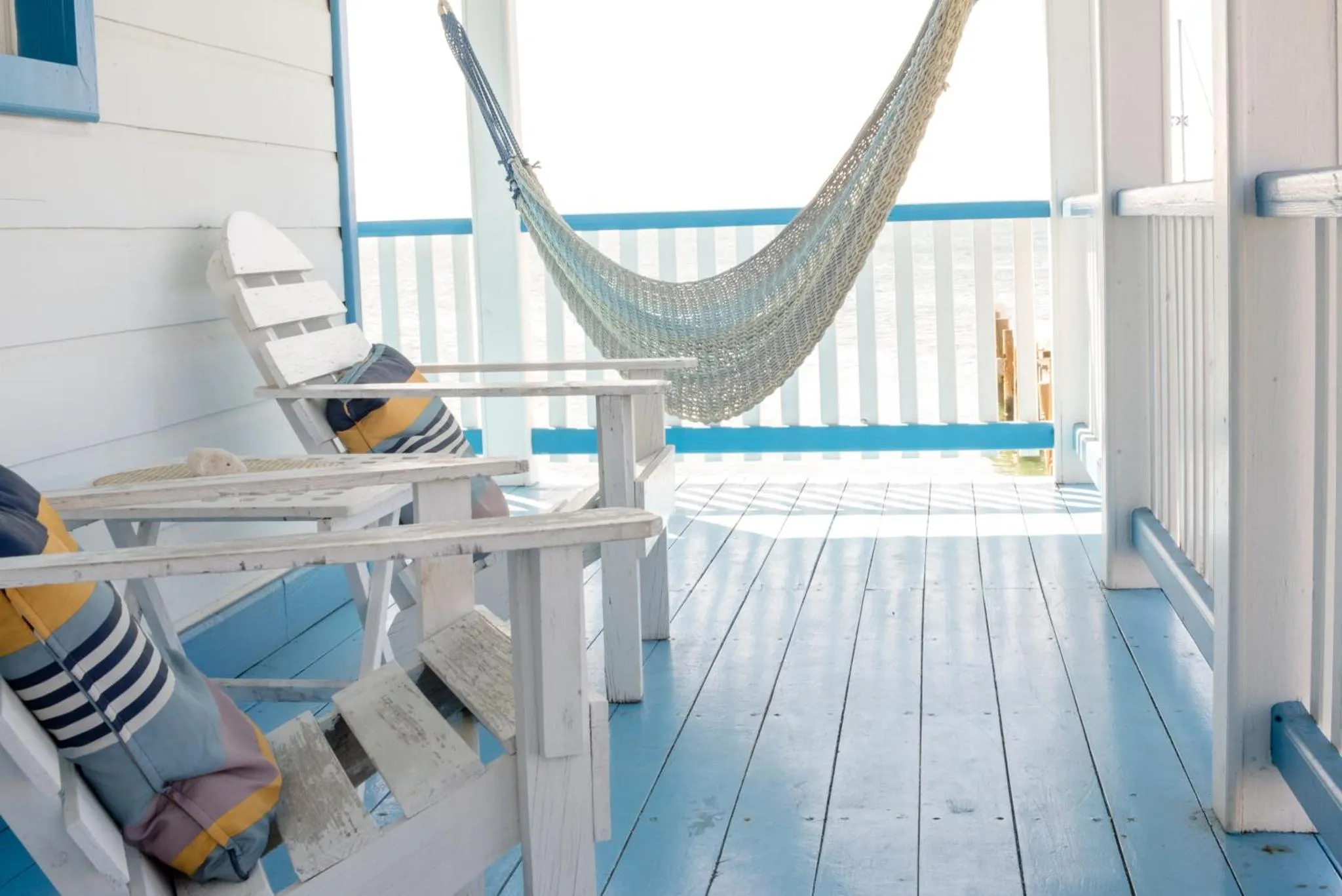 Terrasse en bois avec chaises longues et hamac face à la mer.