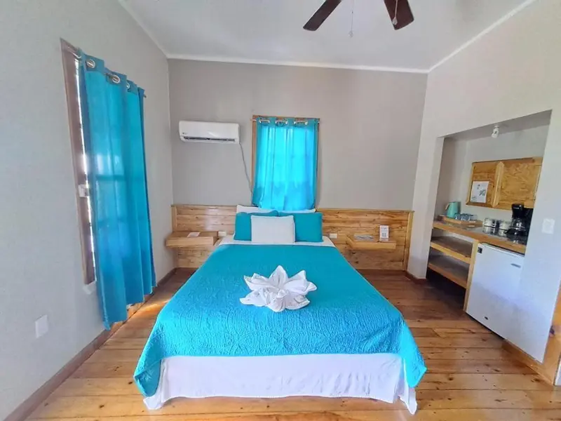 Une chambre lumineuse avec un lit recouvert d'une courtepointe turquoise et un coin cuisine.