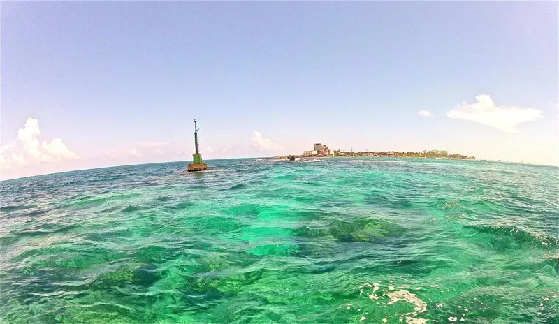 Vue d'une eau turquoise avec une bouée verte au loin et une côte rocheuse.