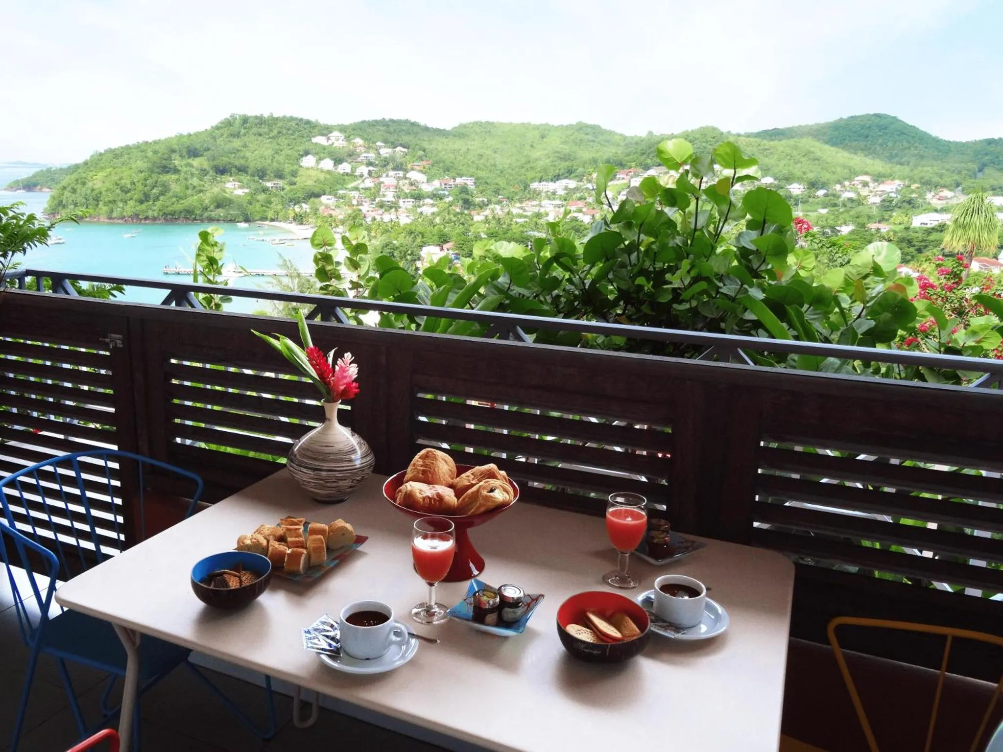 Une table est dressée pour le petit-déjeuner sur une terrasse avec vue sur la mer et la végétation.