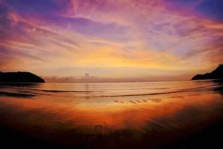 Coucher de soleil sur une plage tropicale avec des reflets orangés sur l'eau.