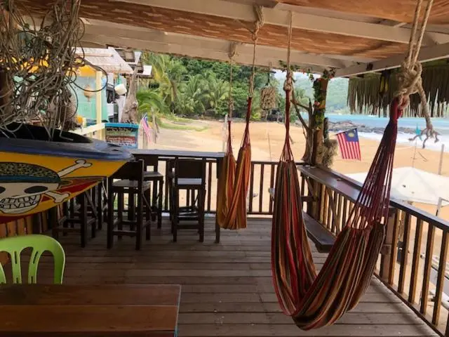 Terrasse ombragée avec des hamacs et des tables en bois donnant sur une plage.