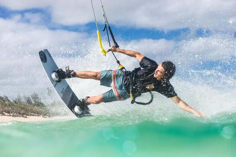Un homme pratique le kitesurf sur une eau turquoise et agitée.