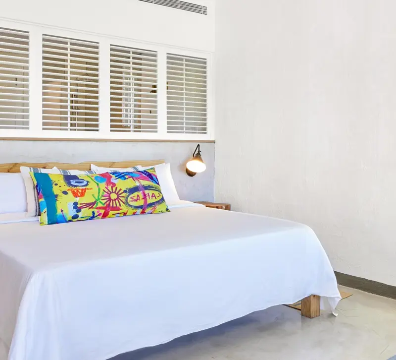 Un lit blanc avec un oreiller coloré dans une chambre lumineuse.