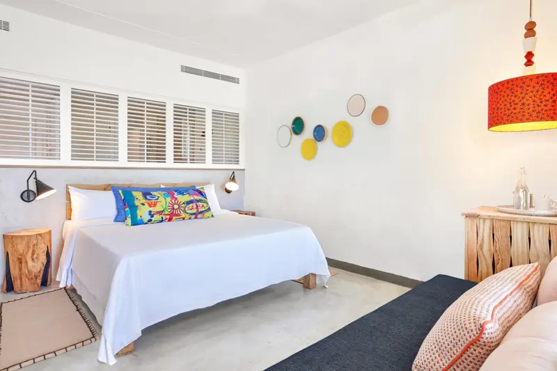 Une chambre lumineuse avec un grand lit recouvert de blanc et des touches de couleurs vives.