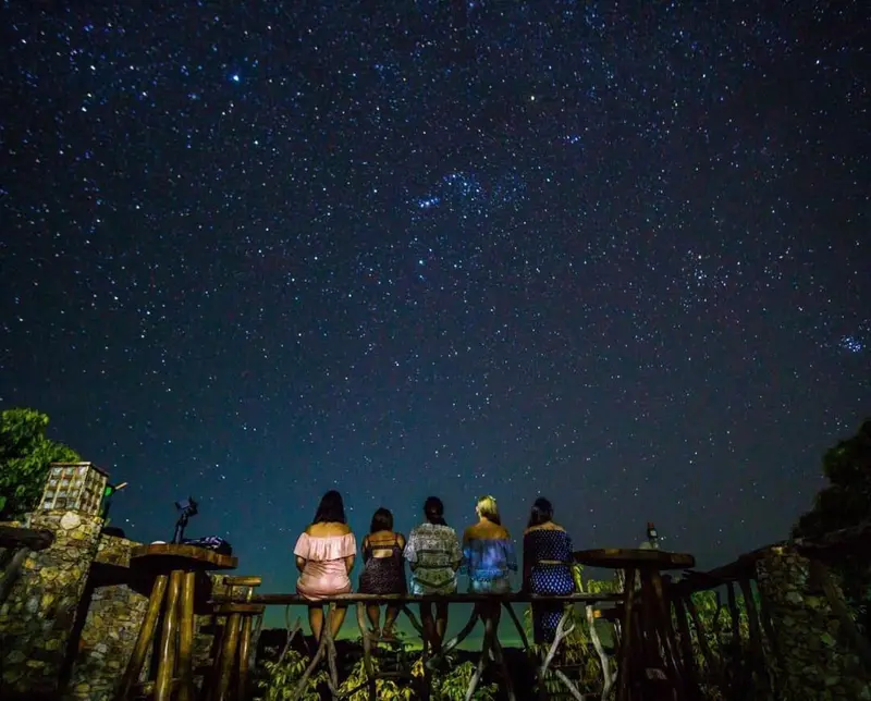 Quatre personnes sont assises sur une rambarde, contemplant un ciel étoilé.