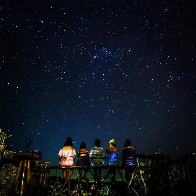 Quatre personnes sont assises sur une rambarde, contemplant un ciel étoilé.