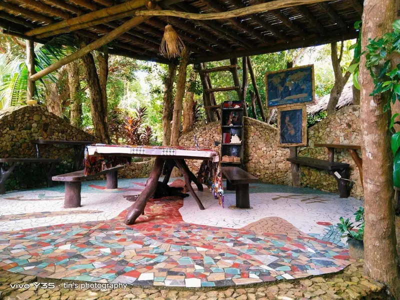Une table en bois rustique se trouve sur un sol mosaïque coloré dans un espace extérieur ombragé.