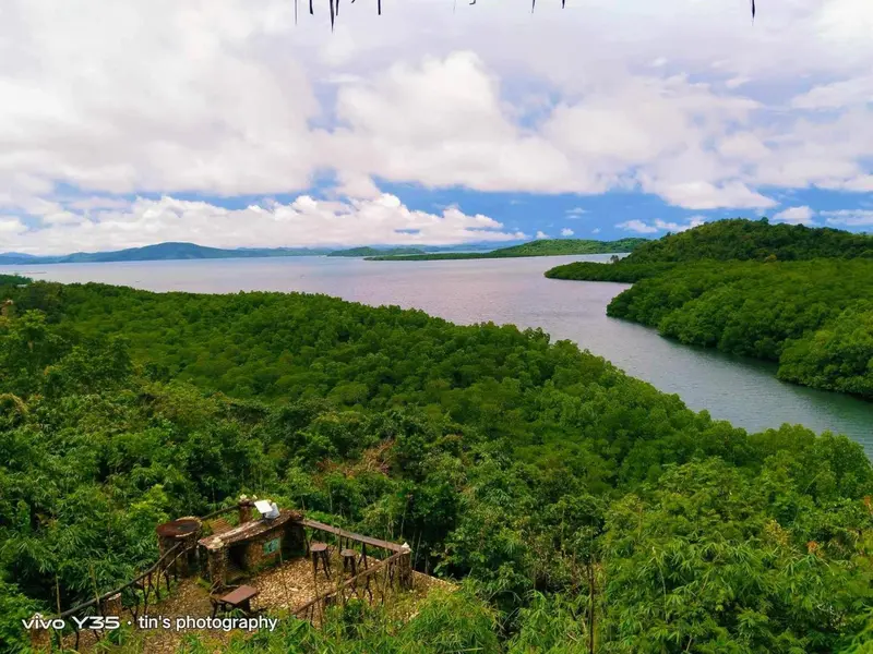 Vue aérienne d'une baie bordée de végétation luxuriante et de collines verdoyantes sous un ciel nuageux.