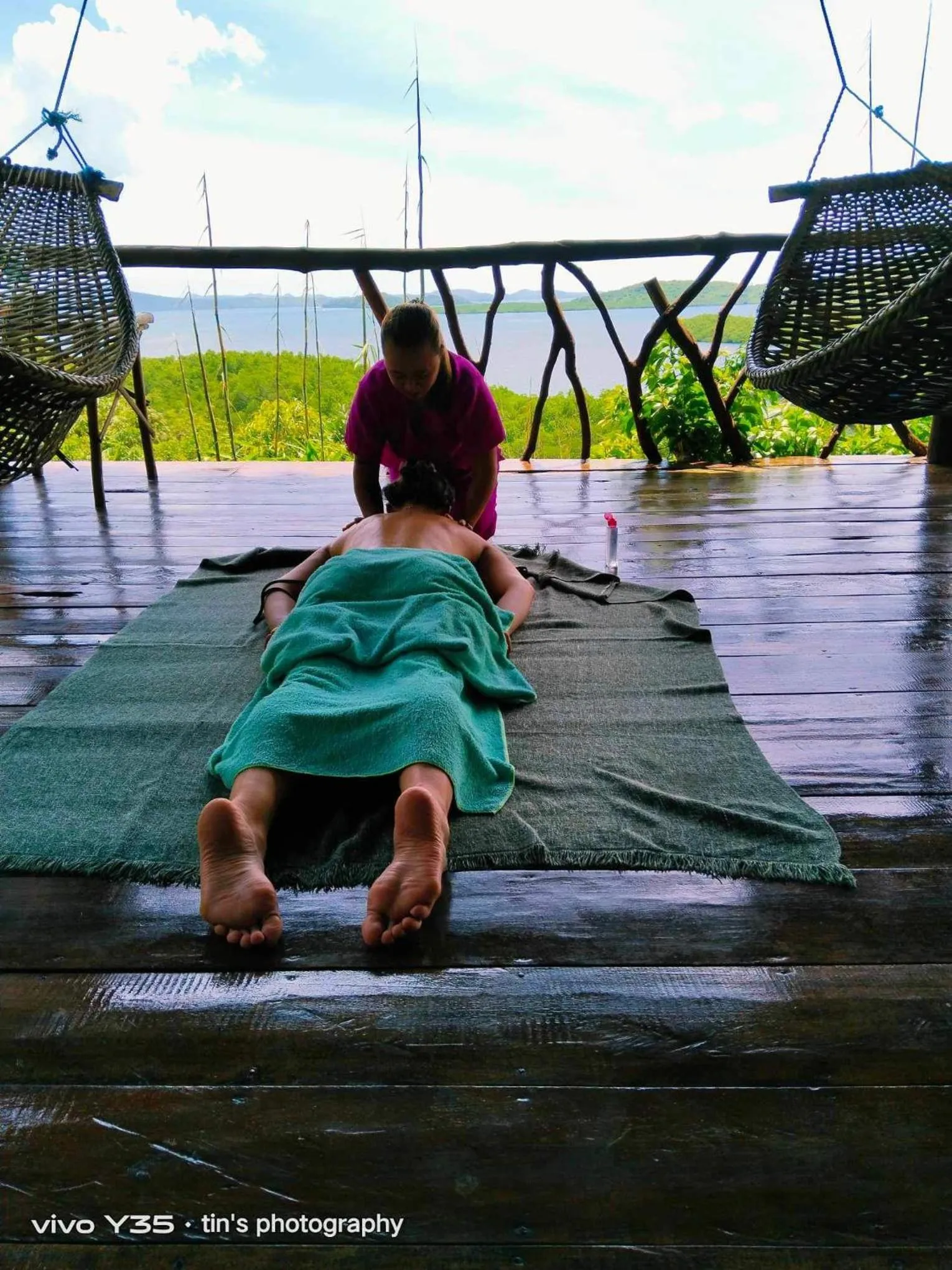 Une personne reçoit un massage sur une terrasse en bois face à la mer.