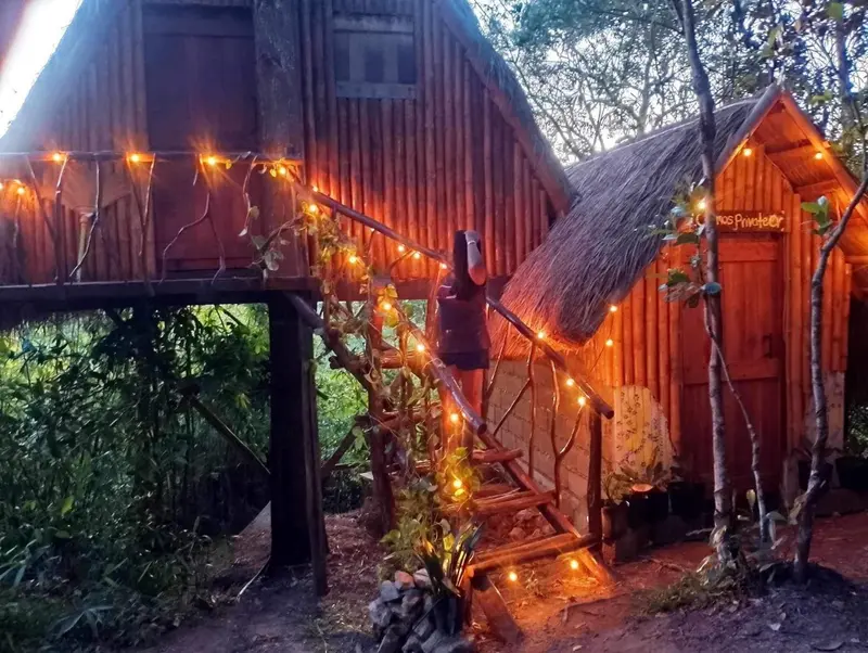 Petite cabane en bois sur pilotis illuminée de guirlandes lumineuses.
