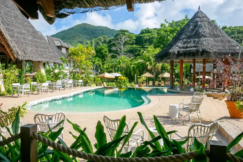 Une piscine turquoise bordée de chaises longues et de végétation luxuriante.