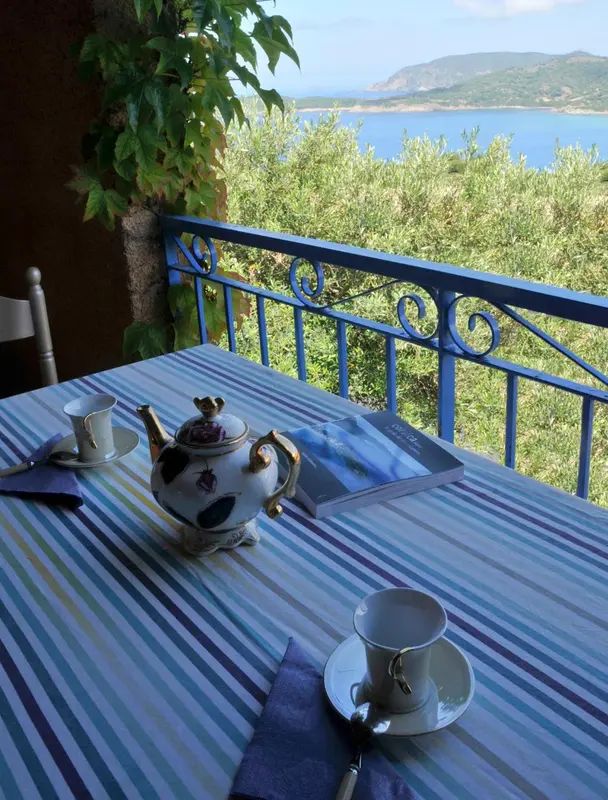 Une table avec une théière et des tasses est mise en scène sur une terrasse ensoleillée.