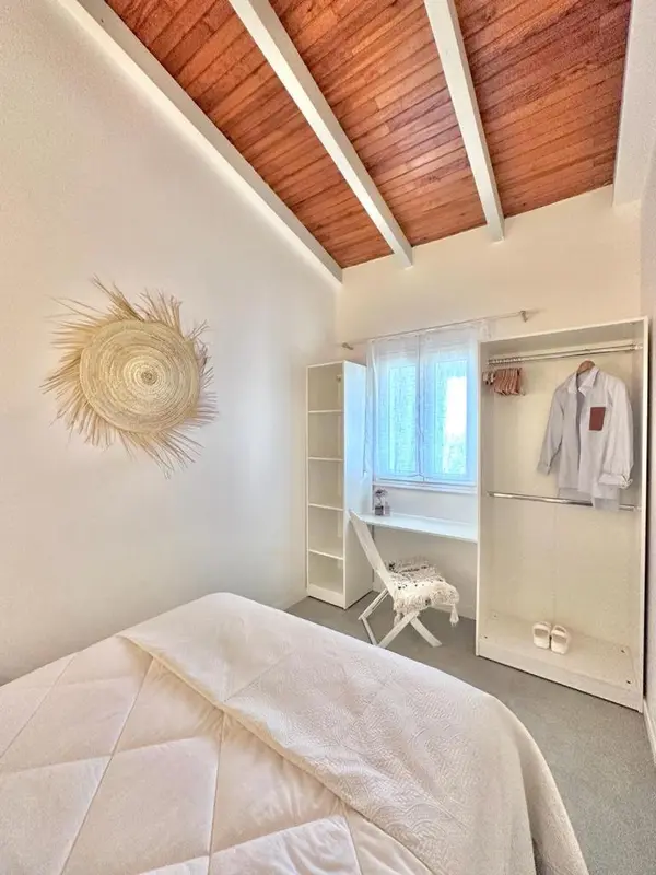 Une chambre lumineuse avec un lit recouvert d'une couverture blanche et une décoration murale en fibres naturelles.