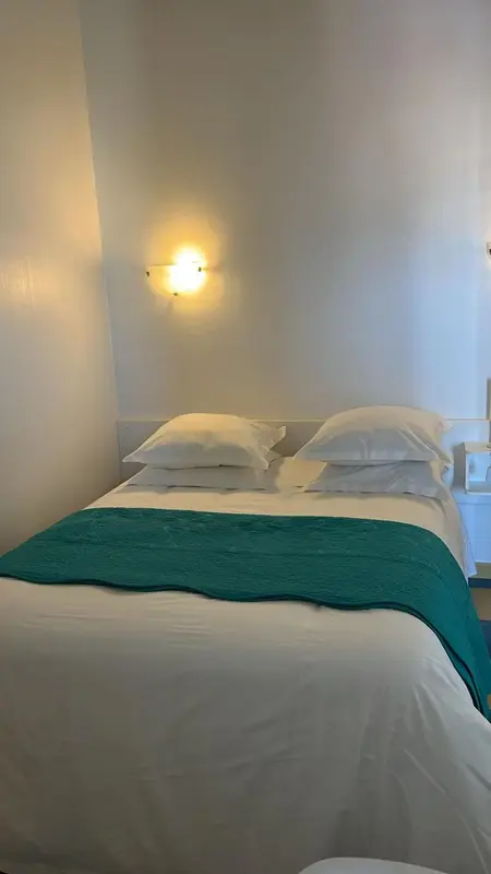Un lit double recouvert d'une couverture turquoise dans une chambre lumineuse.