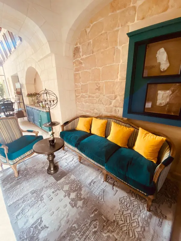 Un canapé turquoise et des fauteuils sont disposés dans un espace intérieur décoré de pierres apparentes.