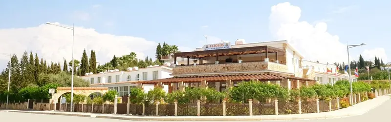 Bâtiment blanc avec une terrasse ombragée et des drapeaux flottant au vent.