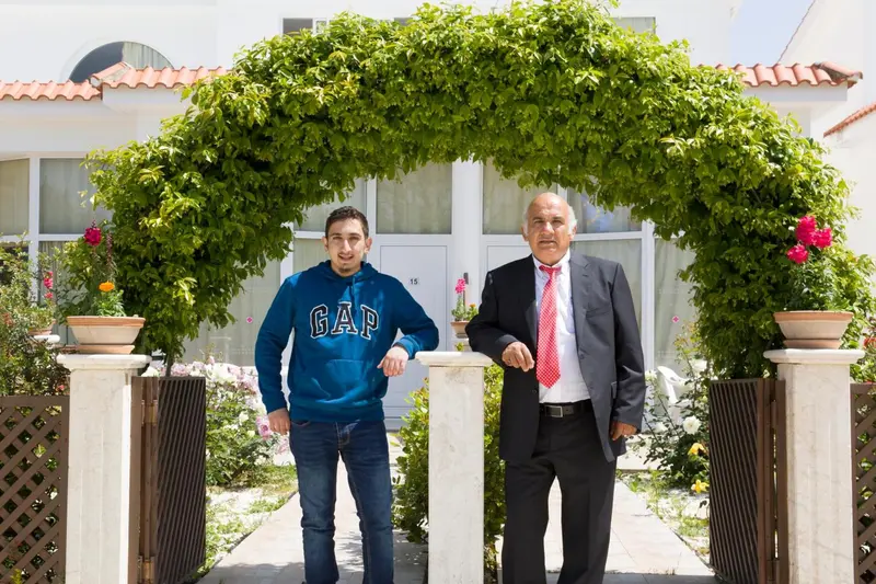 Deux hommes se tiennent devant une entrée ornée de plantes.