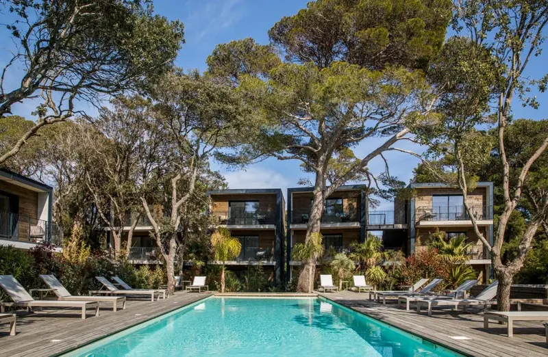 Une piscine turquoise bordée de transats devant des bâtiments modernes.
