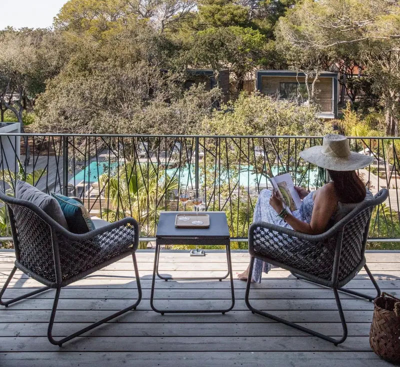 Une personne lit sur une terrasse avec des fauteuils et une table basse.