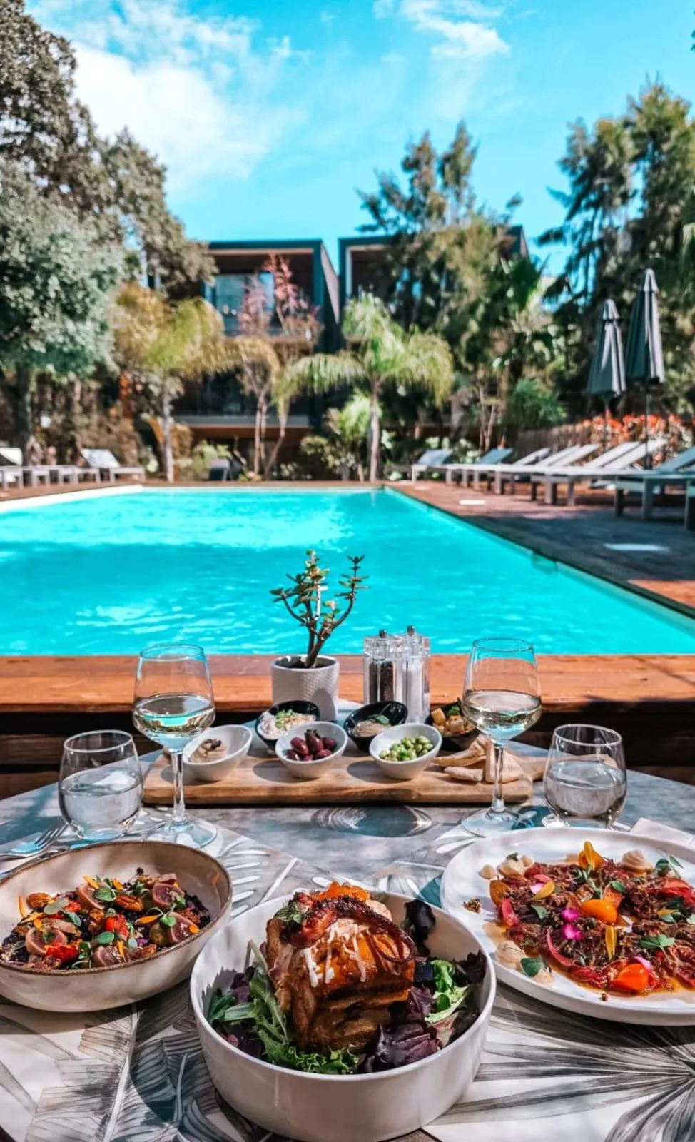 Une table dressée avec des plats et des boissons en terrasse, face à une piscine.