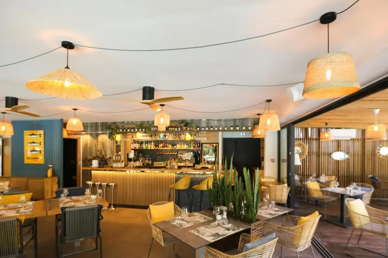 Une salle de restaurant lumineuse avec un comptoir de bar et des tables disposées sur une terrasse.