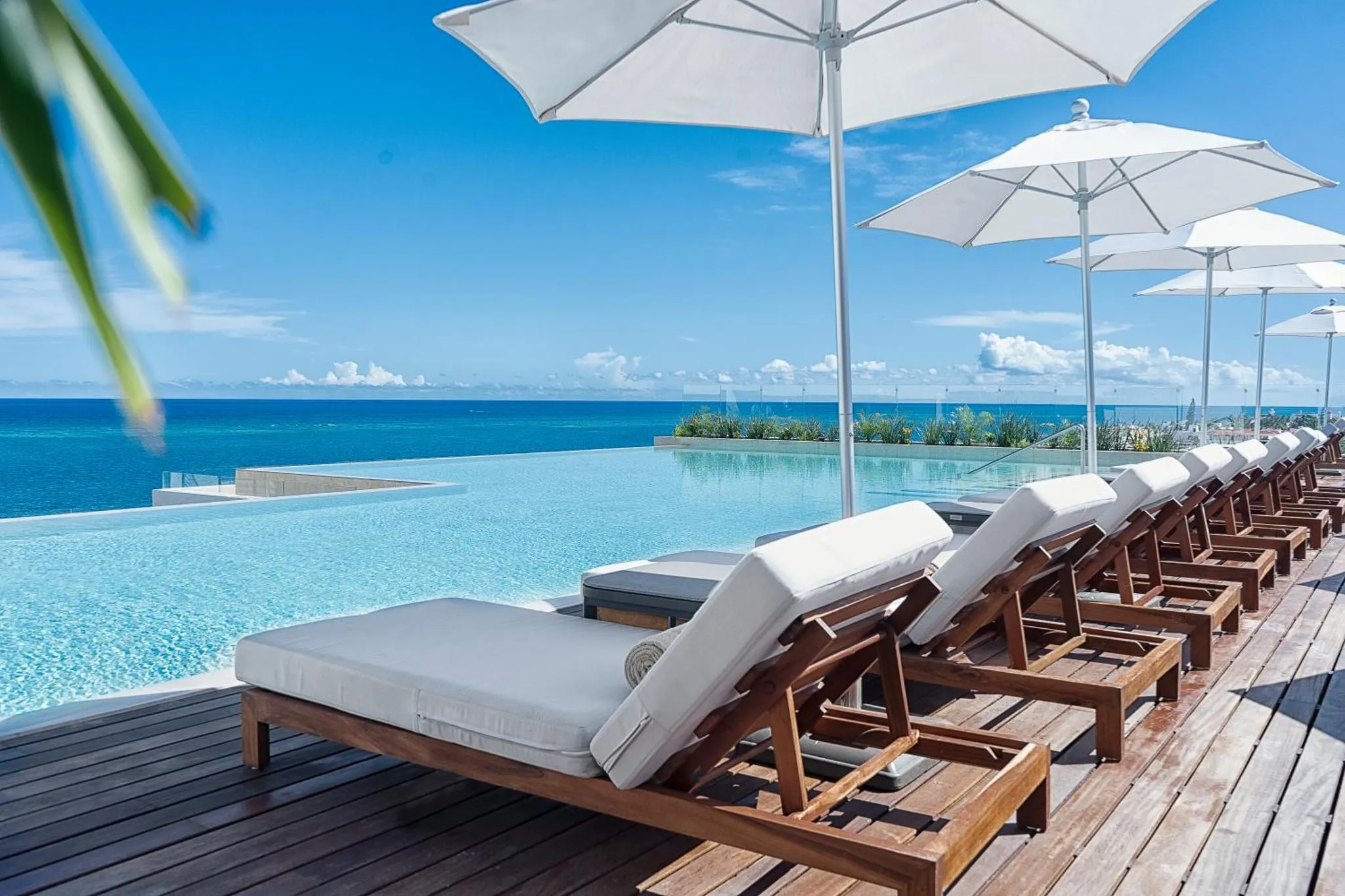 Transats blancs alignés au bord d'une piscine à débordement avec vue sur la mer.