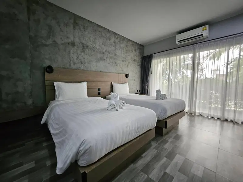 Chambre lumineuse avec deux lits simples et rideaux blancs.