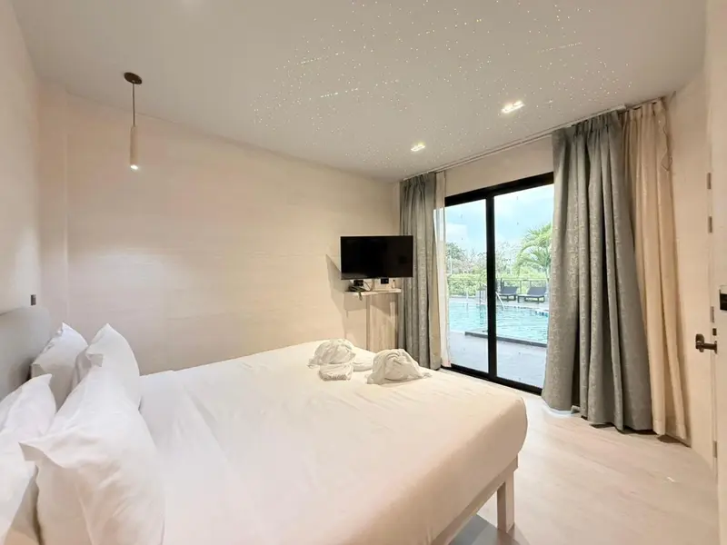 Une chambre lumineuse avec un grand lit et un accès à une piscine.