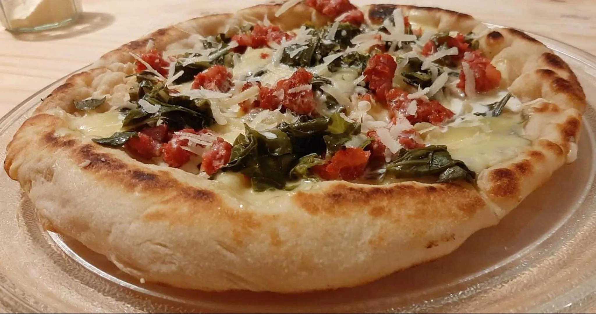 Une pizza aux légumes et au fromage est présentée sur une assiette en verre.