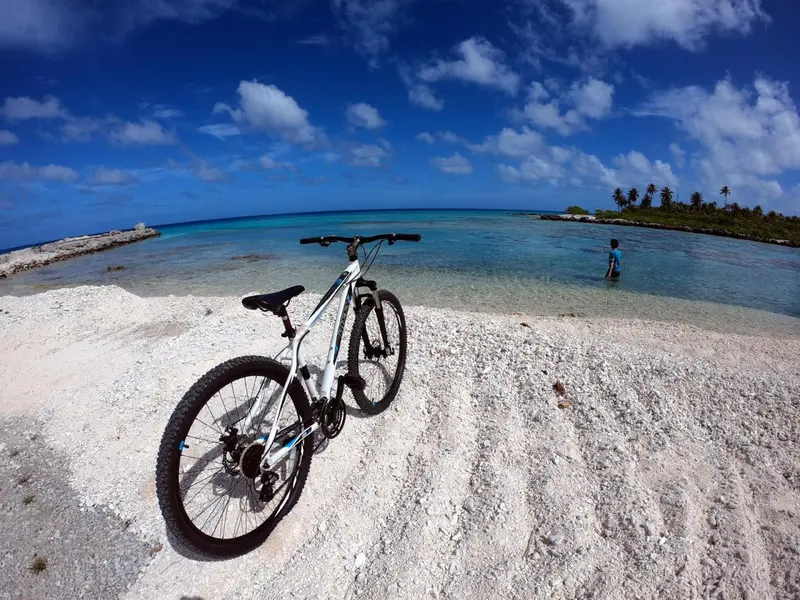 Un vélo est garé sur un rivage de sable blanc face à une eau turquoise.