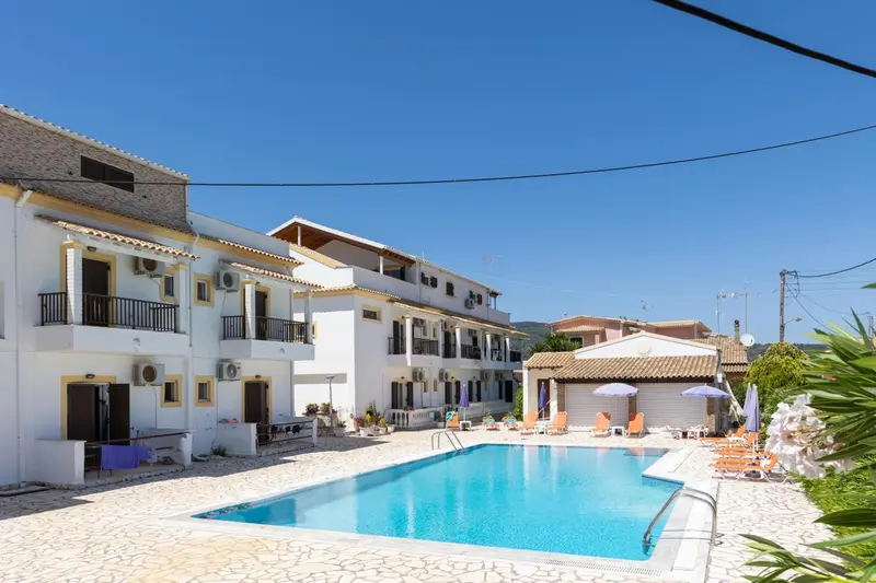 Bâtiment blanc à deux étages avec piscine et transats.