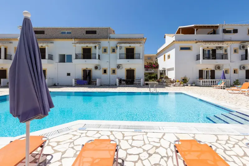 Piscine rectangulaire devant un bâtiment blanc à plusieurs étages avec des balcons.