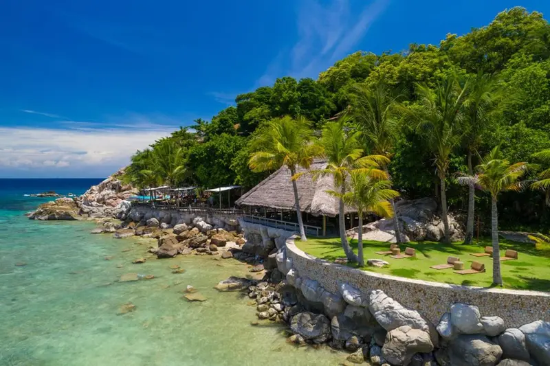 Vue aérienne d'une plage bordée de végétation luxuriante et d'un restaurant en bord de mer.