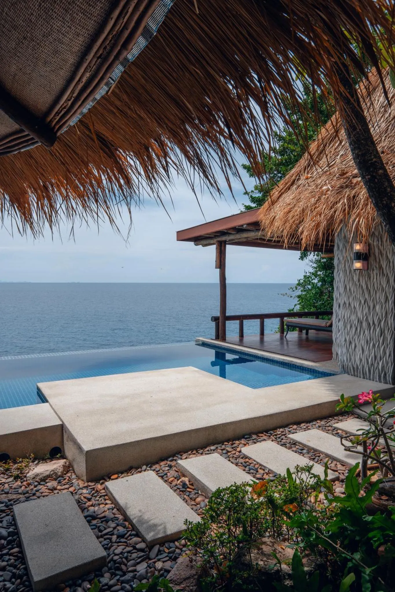 Une piscine à débordement offre une vue sur la mer depuis une terrasse ombragée.