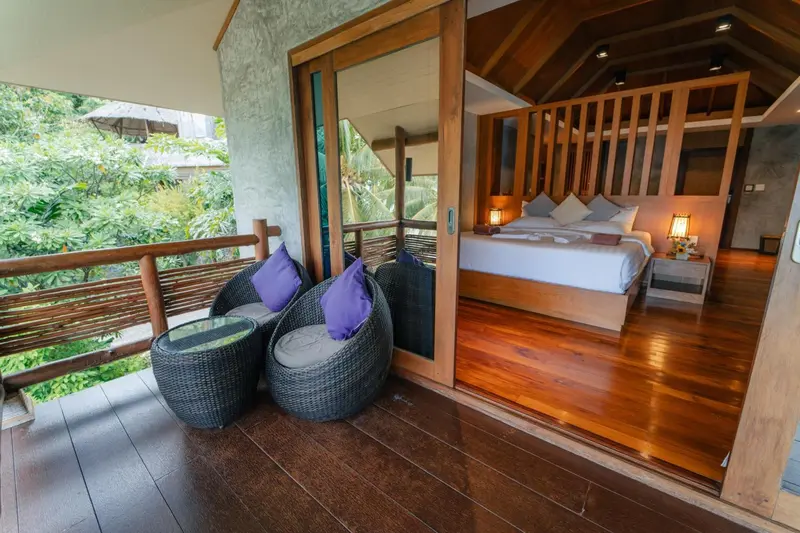 Une chambre lumineuse s'ouvre sur une terrasse aménagée avec des fauteuils.