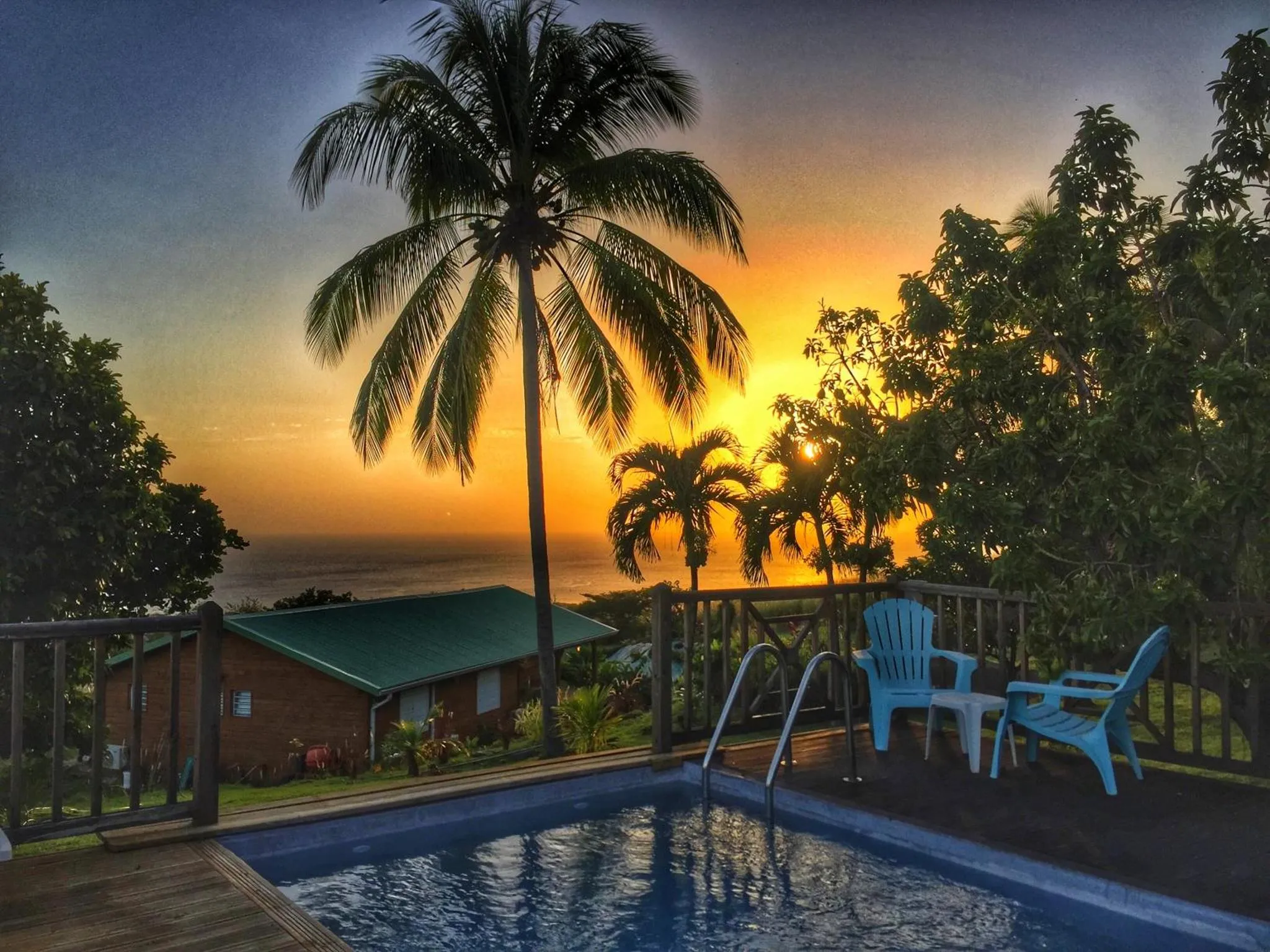 Une piscine au premier plan avec une vue sur la mer et un coucher de soleil flamboyant.