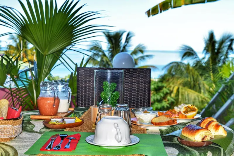 Une table est dressée pour un repas avec des fruits, des viennoiseries et des boissons.