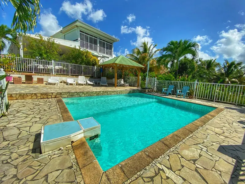 Piscine rectangulaire turquoise entourée d'une terrasse en pierre et de végétation tropicale.