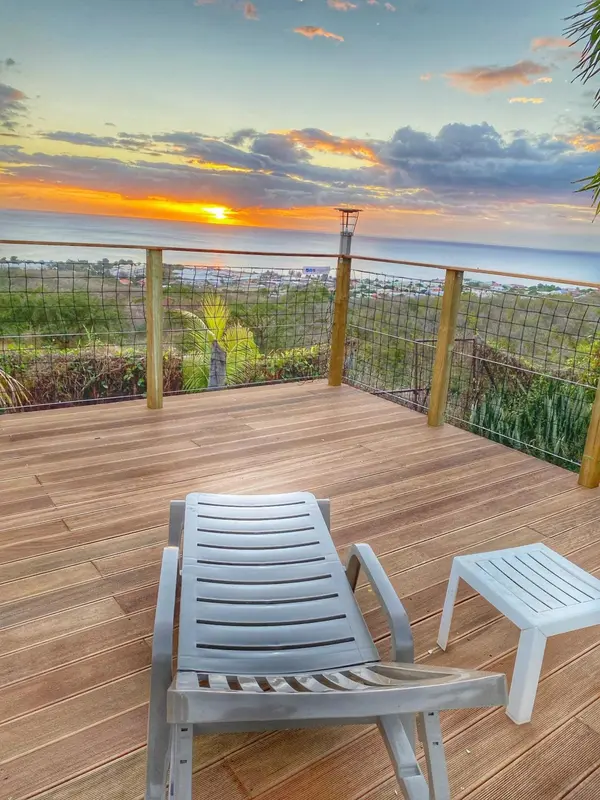 Terrasse en bois avec chaises longues face à la mer au coucher du soleil.