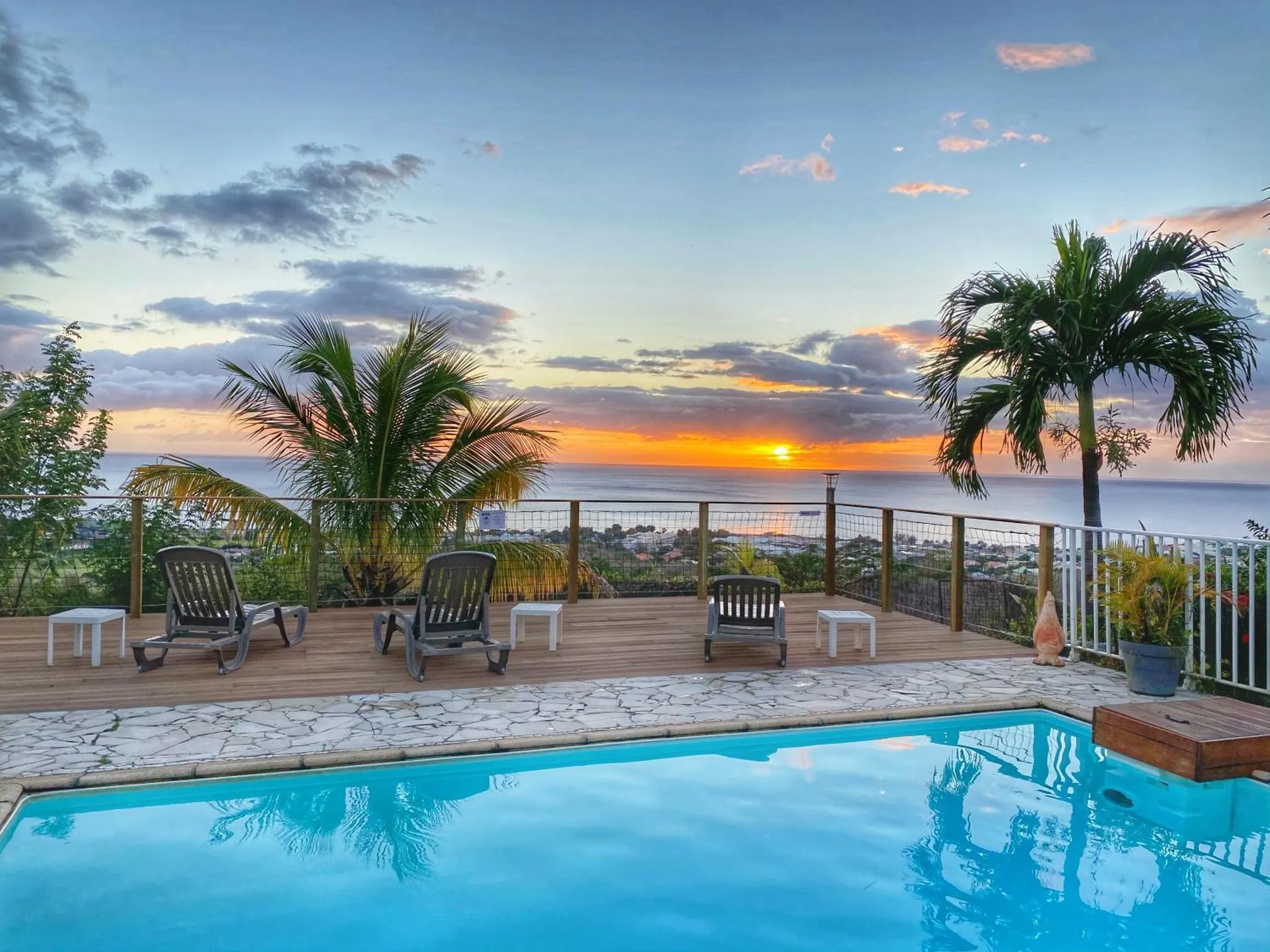 Terrasse avec chaises longues et piscine au bord d'une vue sur la mer au coucher du soleil.