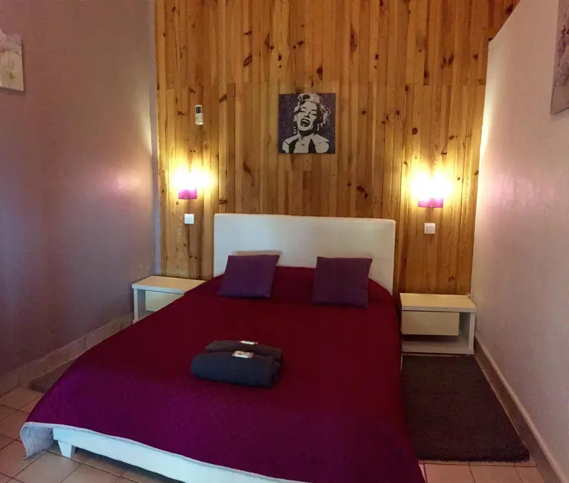 Une chambre avec un grand lit recouvert d'une couverture rouge et d'oreillers violets.