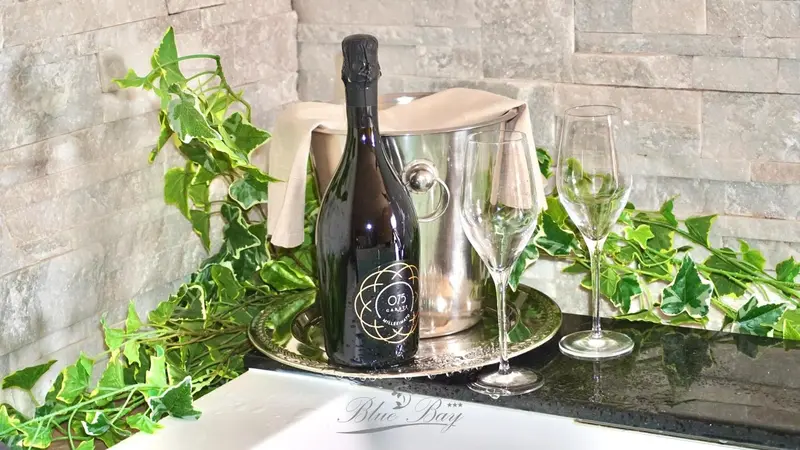 Une bouteille de champagne et deux verres sont présentés sur un plateau décoré de verdure.