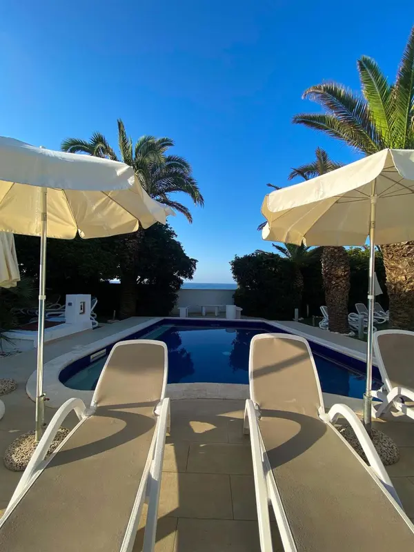 Transats blancs disposés autour d'une piscine rectangulaire sous des parasols.