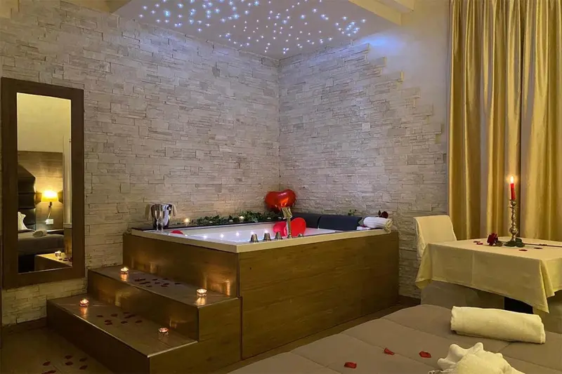 Un bain à remous intégré dans une chambre décorée de pierres, avec des pétales de roses et des bougies.