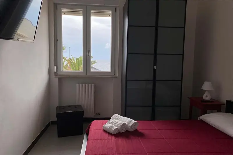 Une chambre avec un lit rouge et une vue sur la mer par la fenêtre.
