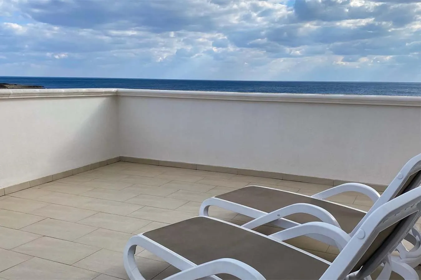 Terrasse carrelée avec transats blancs face à la mer.